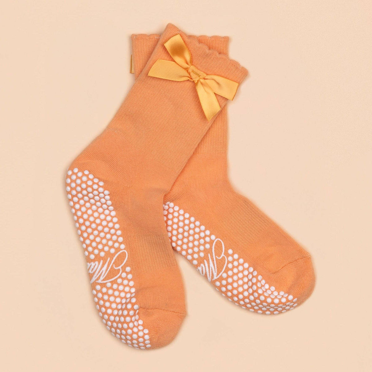 Orange Maison Joie grip socks with satin bow, scalloped cuffs, and white dot soles