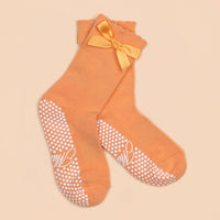 Orange Maison Joie grip socks with satin bow, scalloped cuffs, and white dot soles